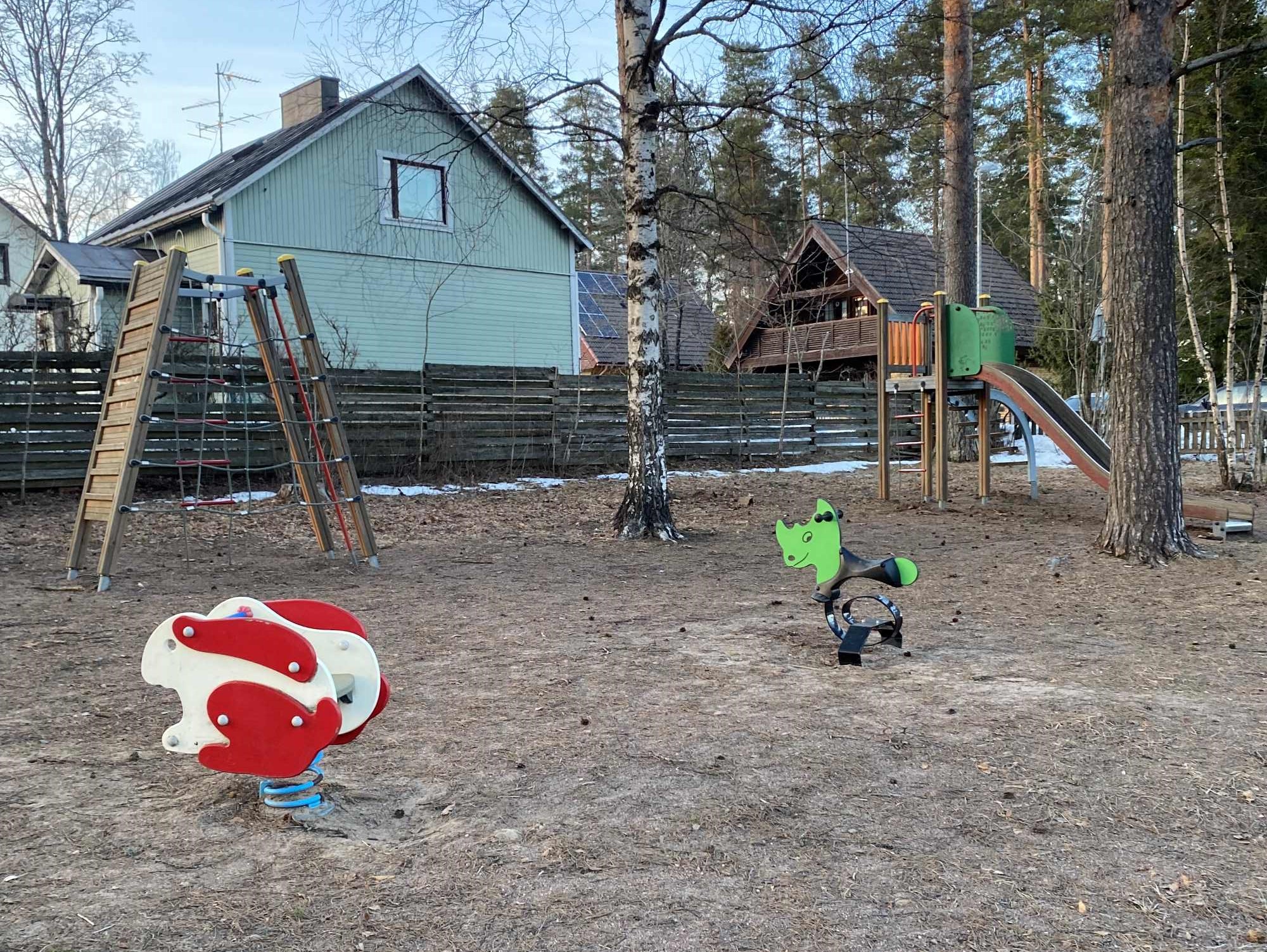 Leikkipuiston leikkilaitteita, takana taloja.